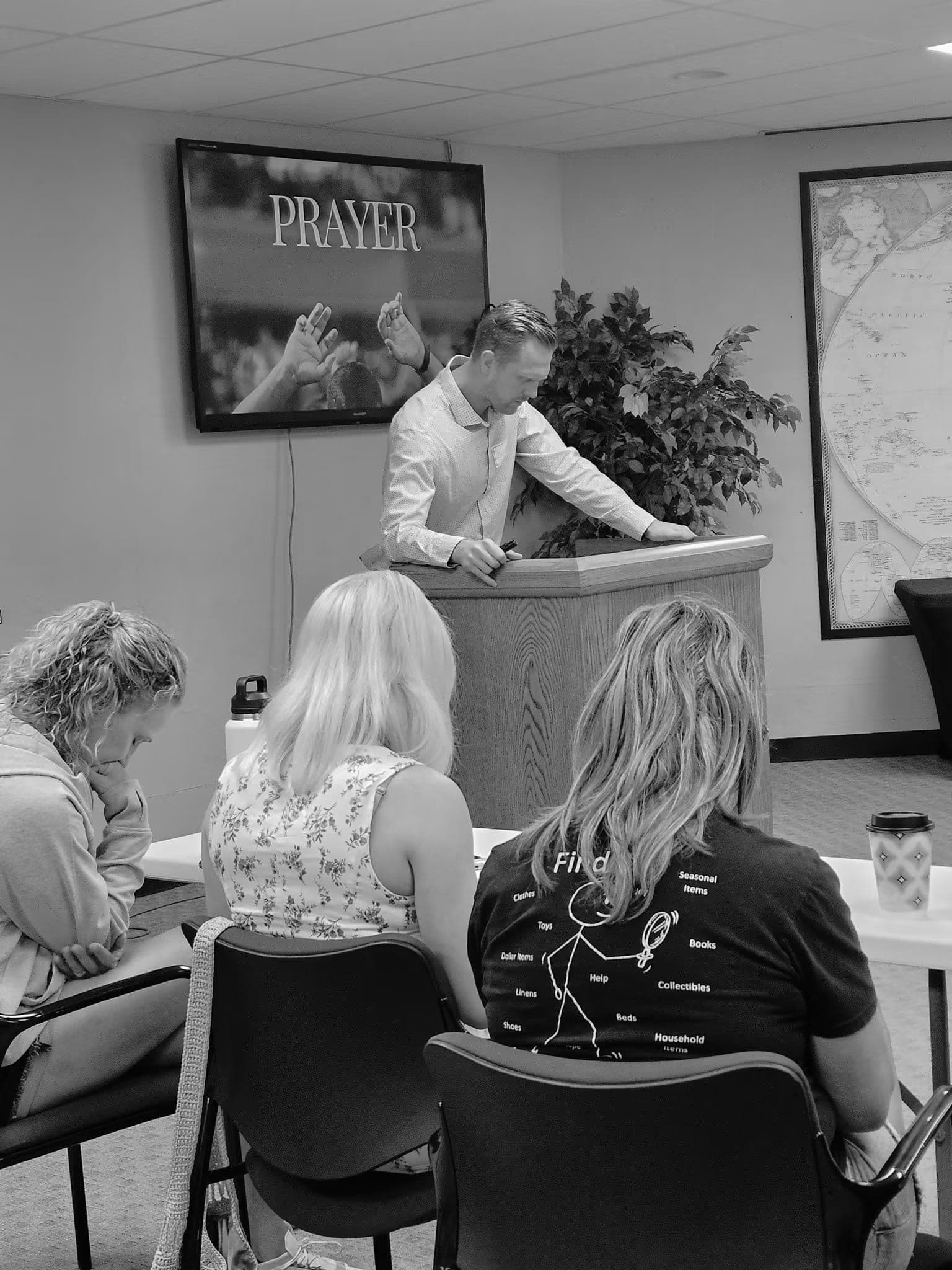 A chamber gathering in prayer, heads bowed around the tables